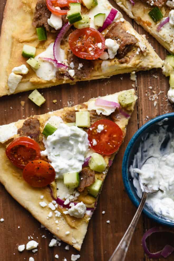 Closeup on slice of gyro pizza topped with tzatziki yogurt sauce.