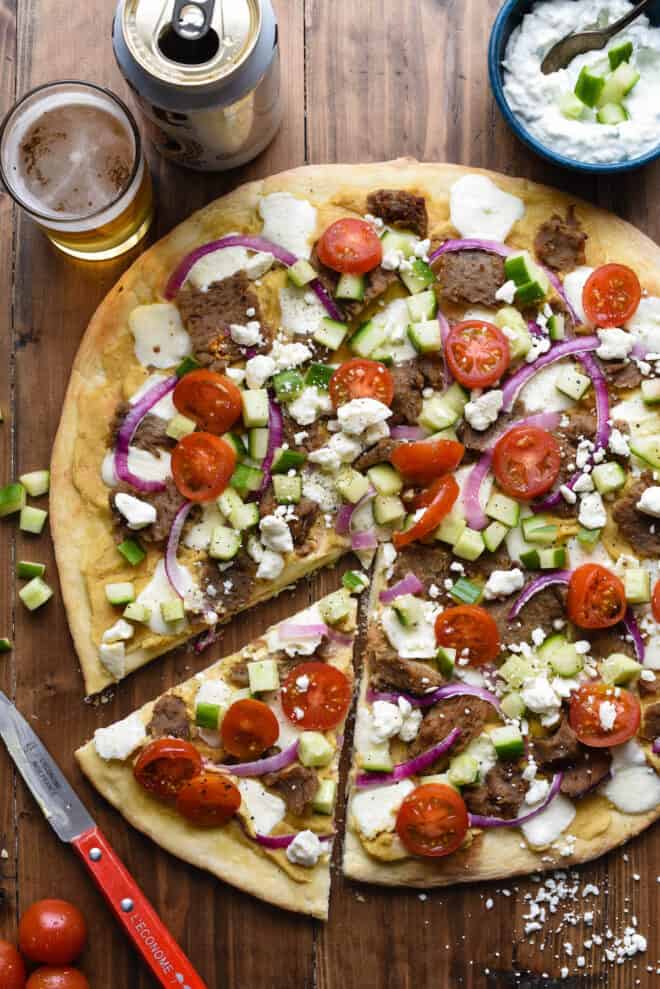Large gyro pizza with one slice cut out on wooden tabletop.