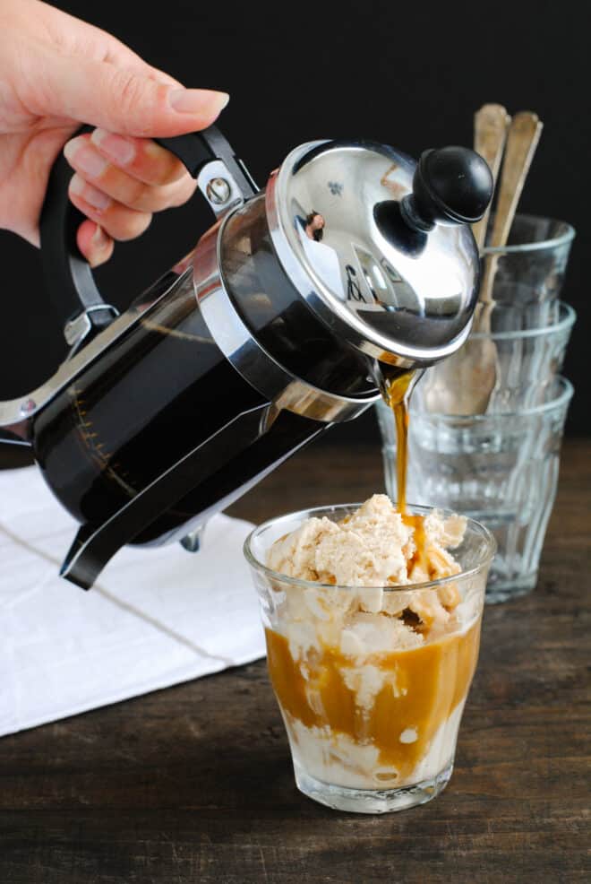 Small glass of ice cream with French pressed coffee being poured over it.