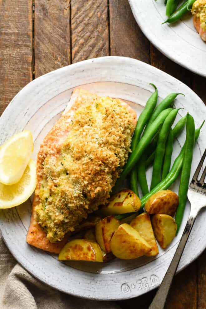Rustic white plate topped with a crab-stuffed salmon recipe, green beans and roasted potato wedges.