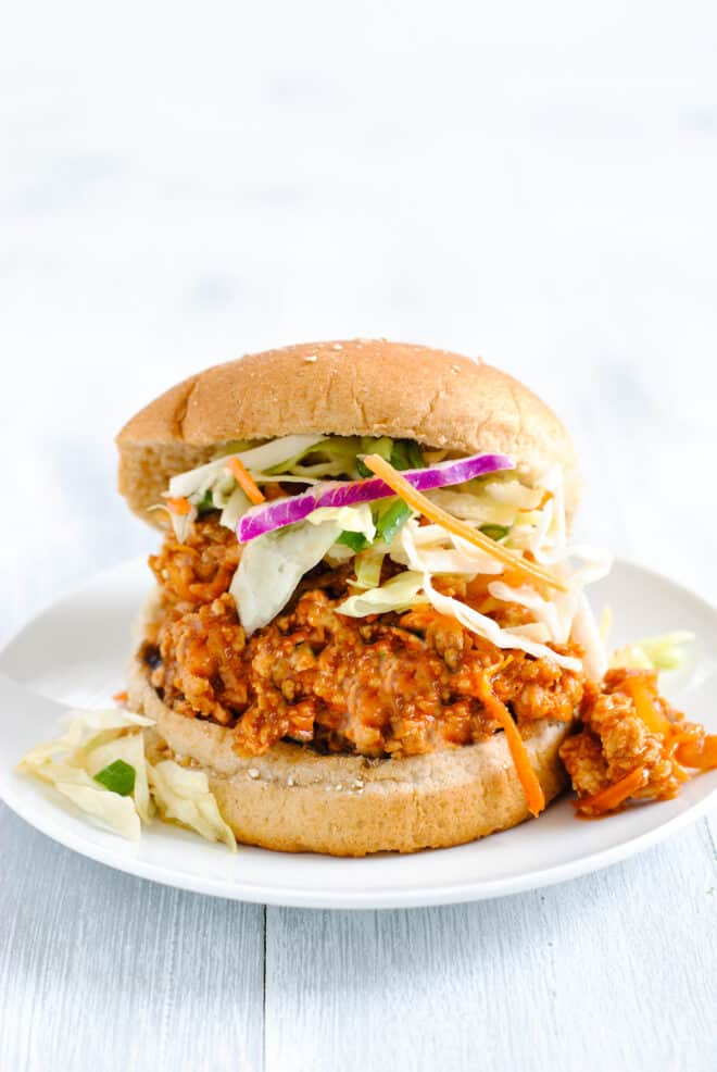 Small white plate topped with hamburger bun filled with chicken sloppy joes and coleslaw.