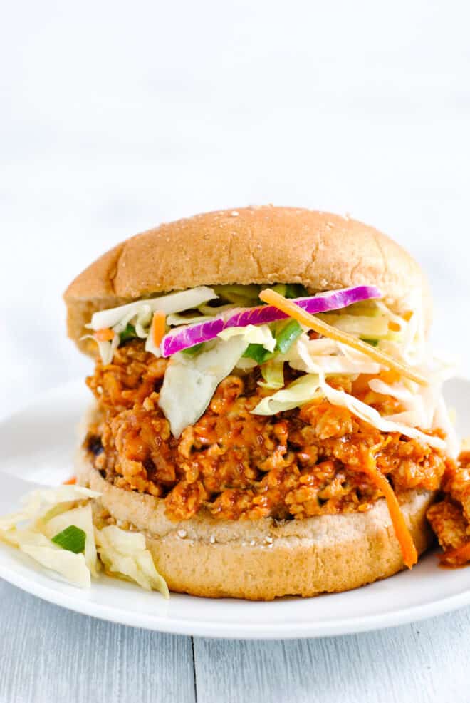 White plate with burger bun filled with loose ground chicken saucy mixture and coleslaw.