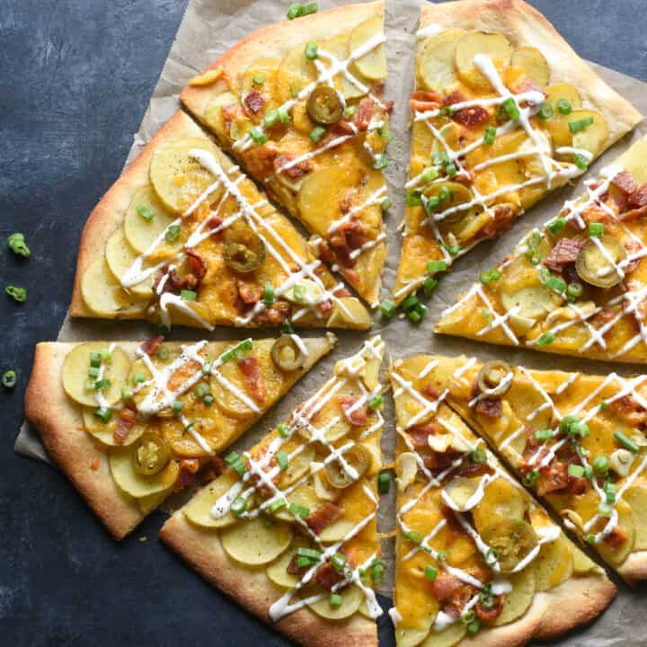 Loaded baked potato pizza drizzled with ranch dressing, on dark surface.