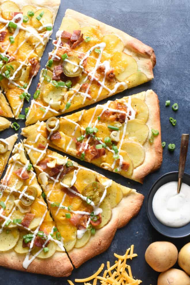 Pizza crust topped with sliced potatoes and bacon, with small bowl of ranch dressing alongside.