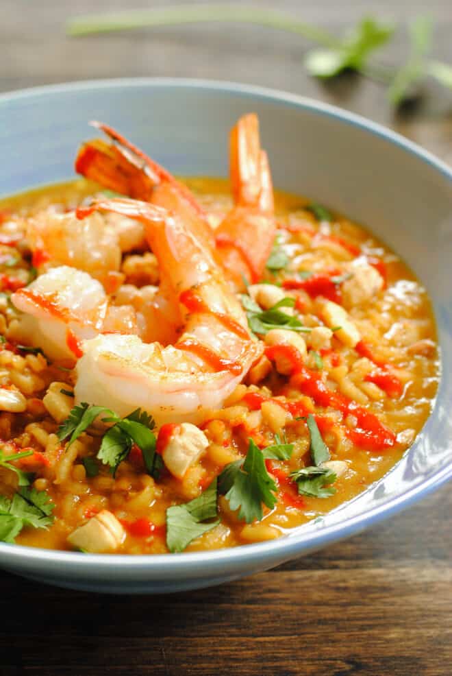 Shallow light blue bowl filled with richly orange colored risotto, topped with three large shrimp.