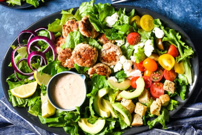 Large platter filled with lettuce, small turkey patties, avocado, croutons, feta cheese, tomatoes and a creamy dressing.
