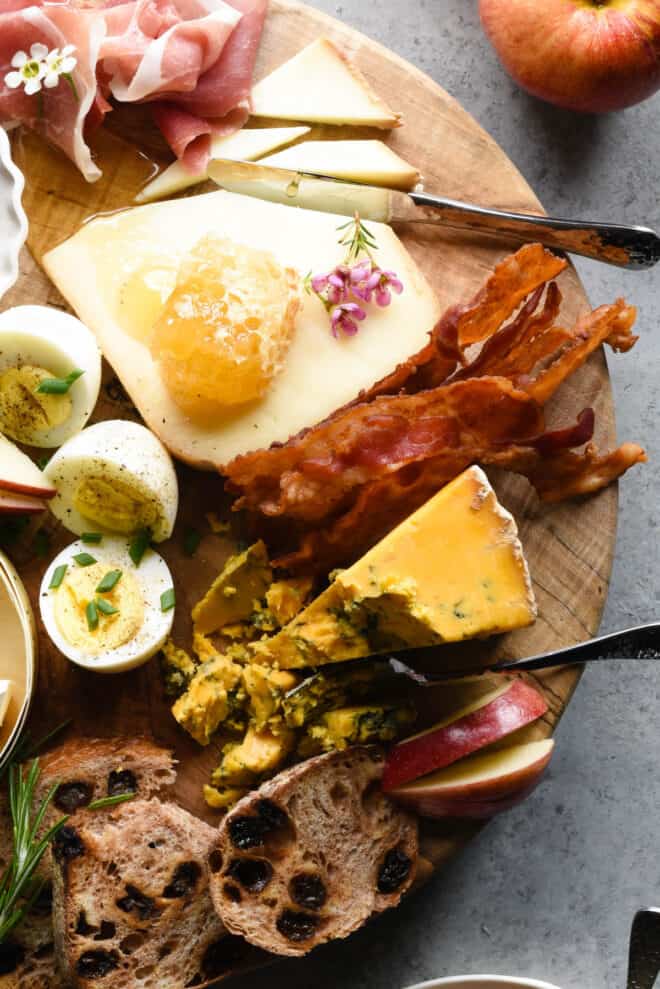 Wooden brunch board topped with cheese, bacon, honeycomb and hard boiled eggs.