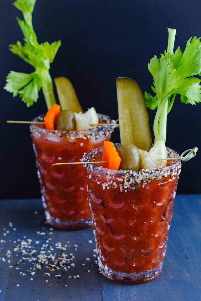 Two textured glasses crusted with bloody mary rim salt and filled with bloody mary mix, pickles, olives and celery.