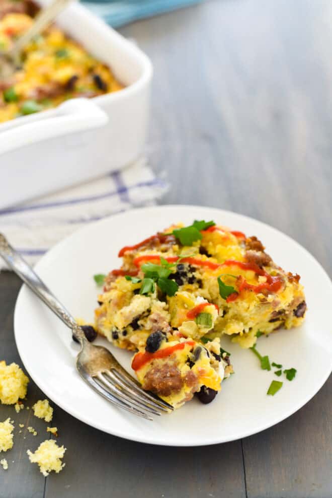 A piece of cornbread breakfast casserole on a small white plate with a fork about to take a bite.