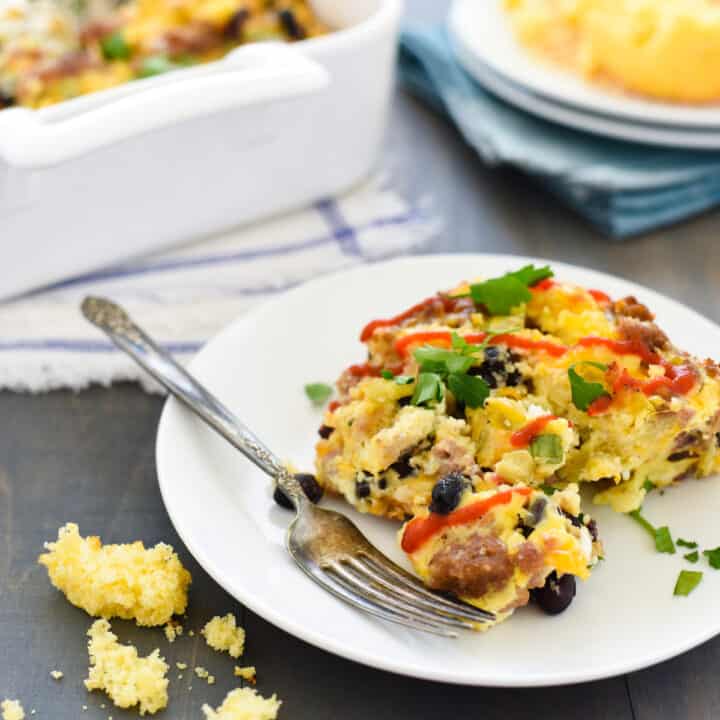 Egg casserole on small white plate. Crumbled cornbread next to plate.