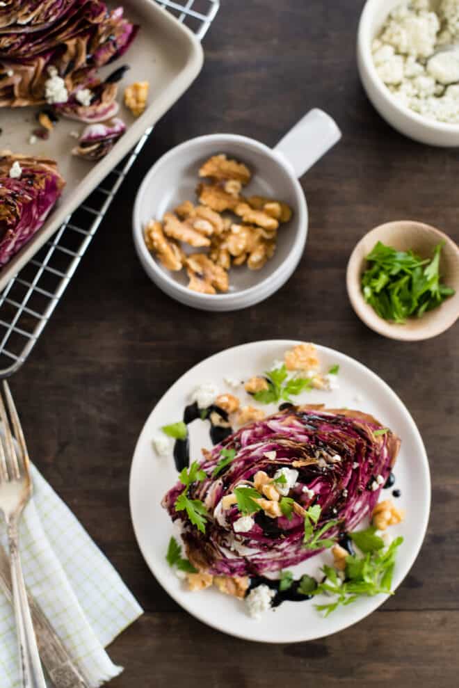 Roasted radicchio wedge salad on white plate, with small bowls of nuts, cheese and herbs nearby.