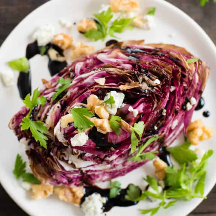 White plate topped with wedge of roasted purple radicchio, topped with cheese, nuts and herbs.