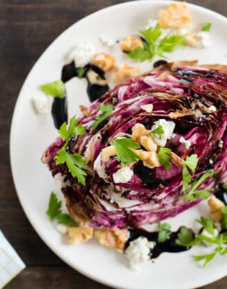 White plate topped with wedge of roasted purple radicchio, topped with cheese, nuts and herbs.