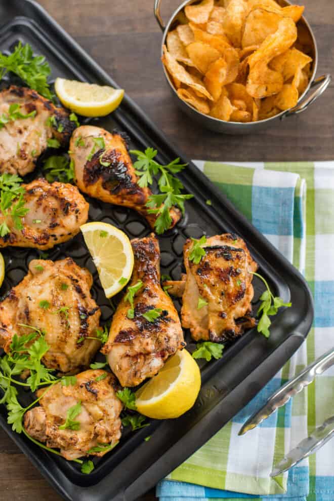 Large black tray of grilled chicken that has been soaked in buttermilk chicken marinade, with potato chips and tongs nearby.