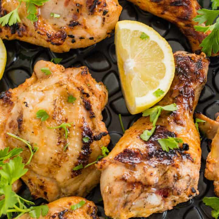 Grilled chicken legs and thighs garnished with lemon wedges and parsley.