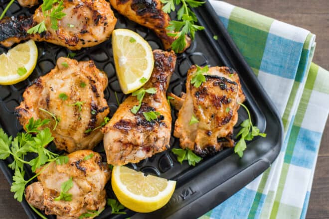 Black tray of buttermilk grilled chicken garnished with parsley and lemon wedges.