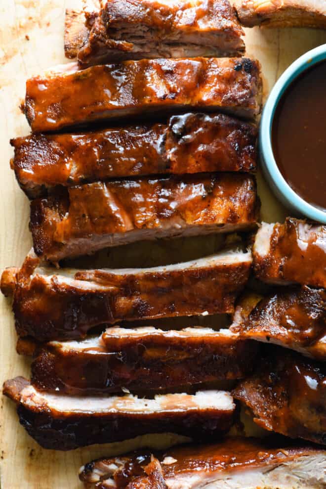 Close up on wooden cutting board with cut crockpot ribs glazed with sauce.