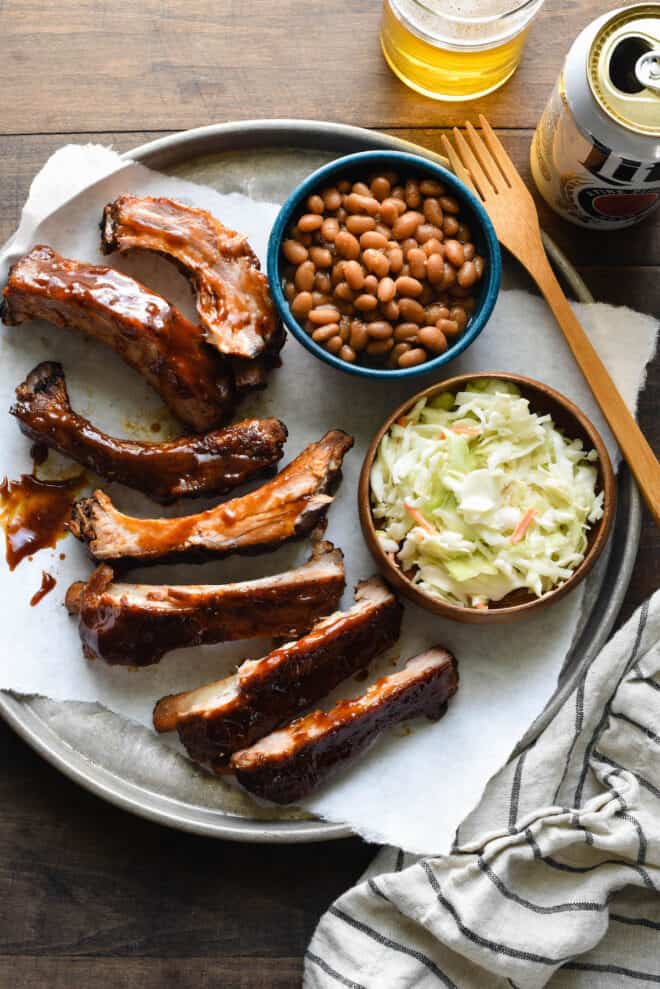A platter with baby back ribs and side dishes for ribs including coleslaw and baked beans.