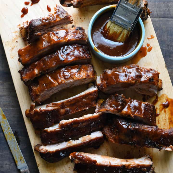 Wooden cutting board with cut racks of crock pot ribs glazed with barbecue sauce.