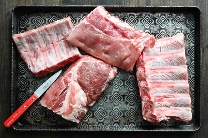 A textured baking pan with four raw sections of rib racks, and a paring knife.