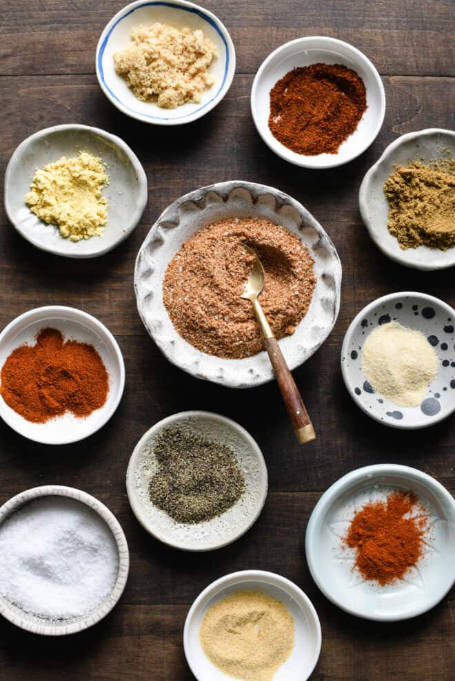 Several small bowls of various ground spices on wooden tabletop.