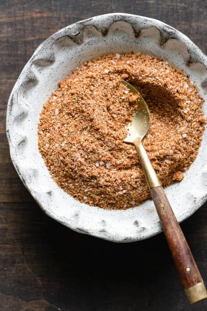 Handmade ceramic bowl filled with a rib rub recipe, with small spoon inserted in it.