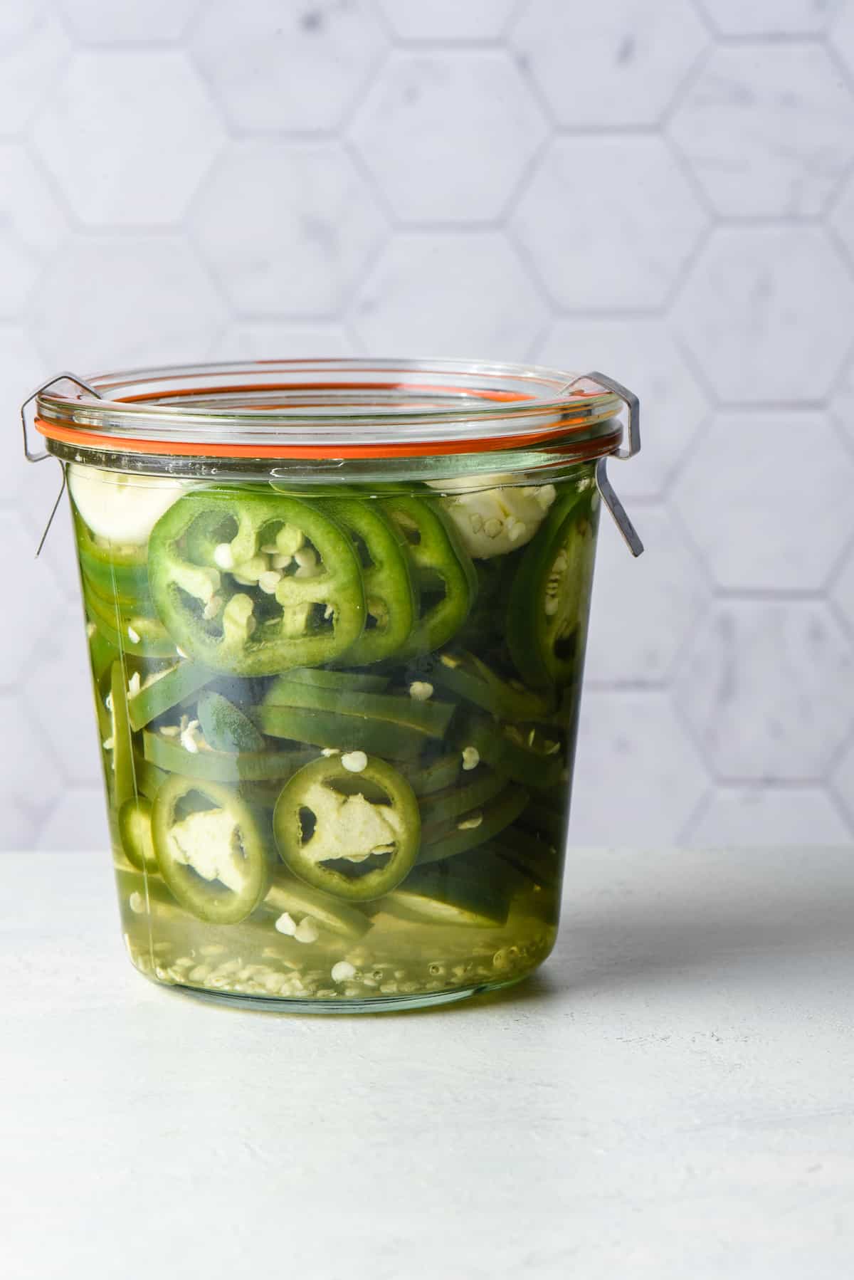 Jar of pickled jalapenos against light background.