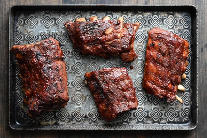 A textured baking pan with four sections of crockpot baby back ribs that have been sauced and lightly charred.