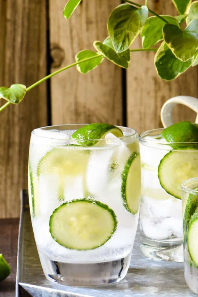 Close up on a White Claw cocktail over ice in a small glass, garnished with limes and cucumber slices.