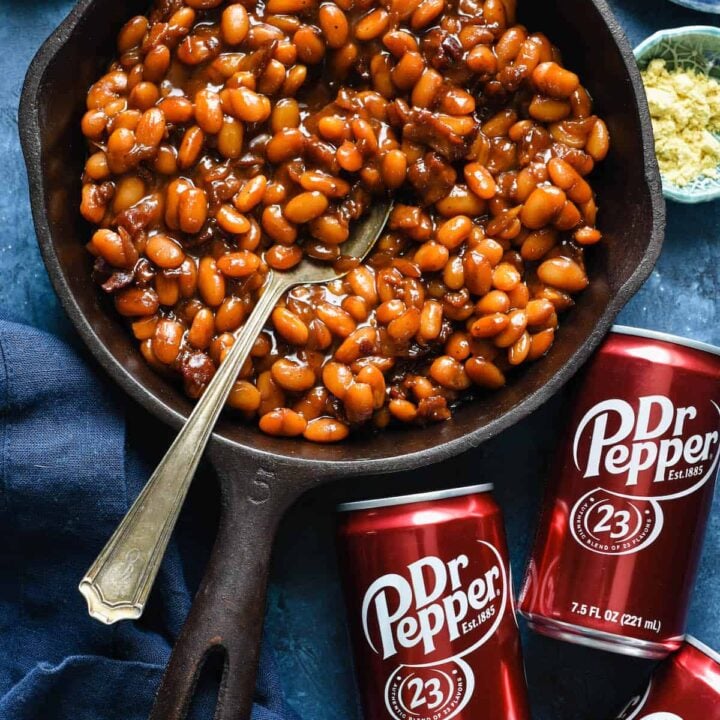 Cast iron skillet filled with baked beans with cans of Dr. Pepper next to skillet.