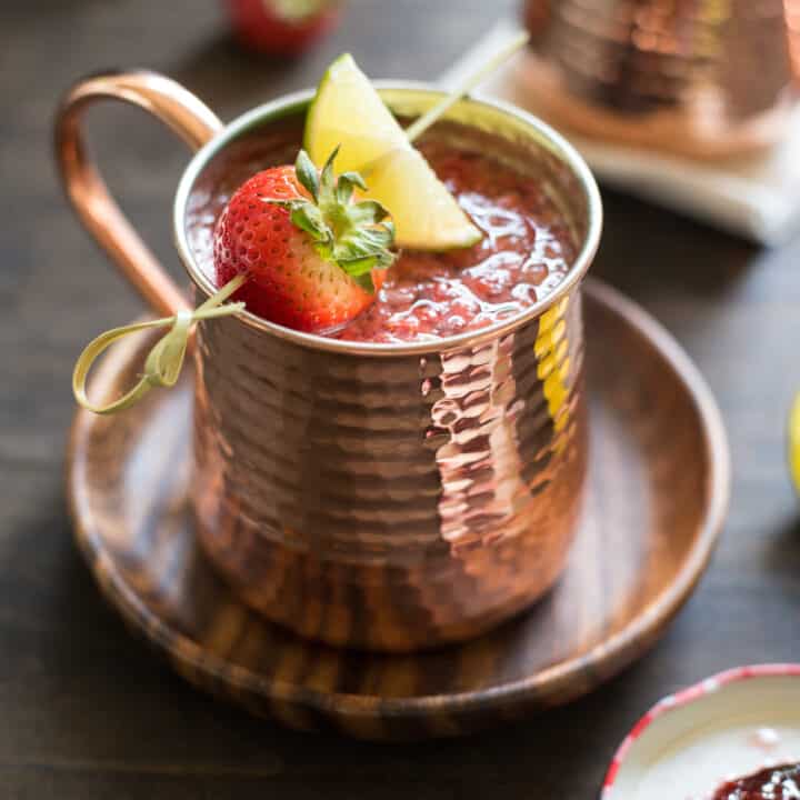 Hammered copper mug filled with strawberry Moscow mule, garnished with a skewer with a strawberry and lime wedge.