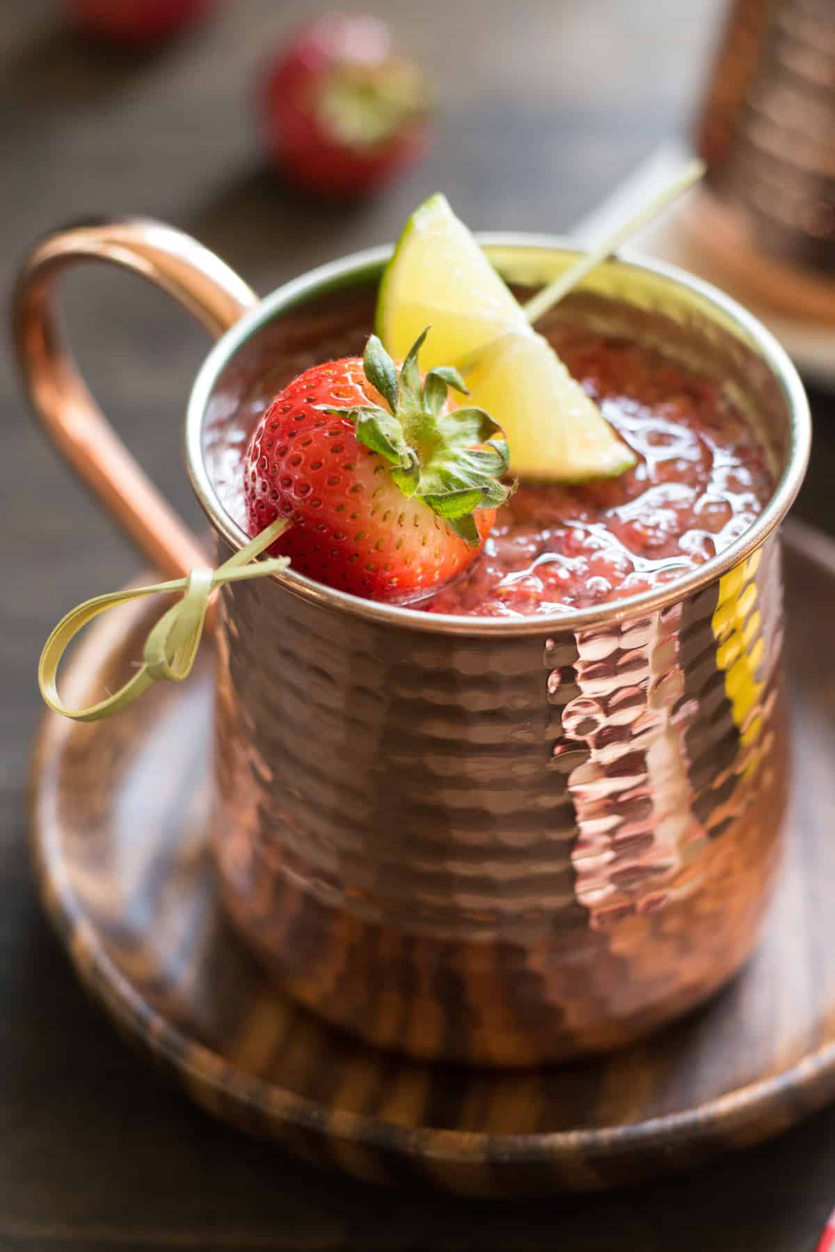 Hammered copper mug filled with strawberry Moscow mule, garnished with a skewer with a strawberry and lime wedge.