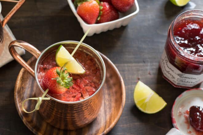 Strawberry cocktail in a copper mug with a skewer of strawberry and lime resting on top of mug.