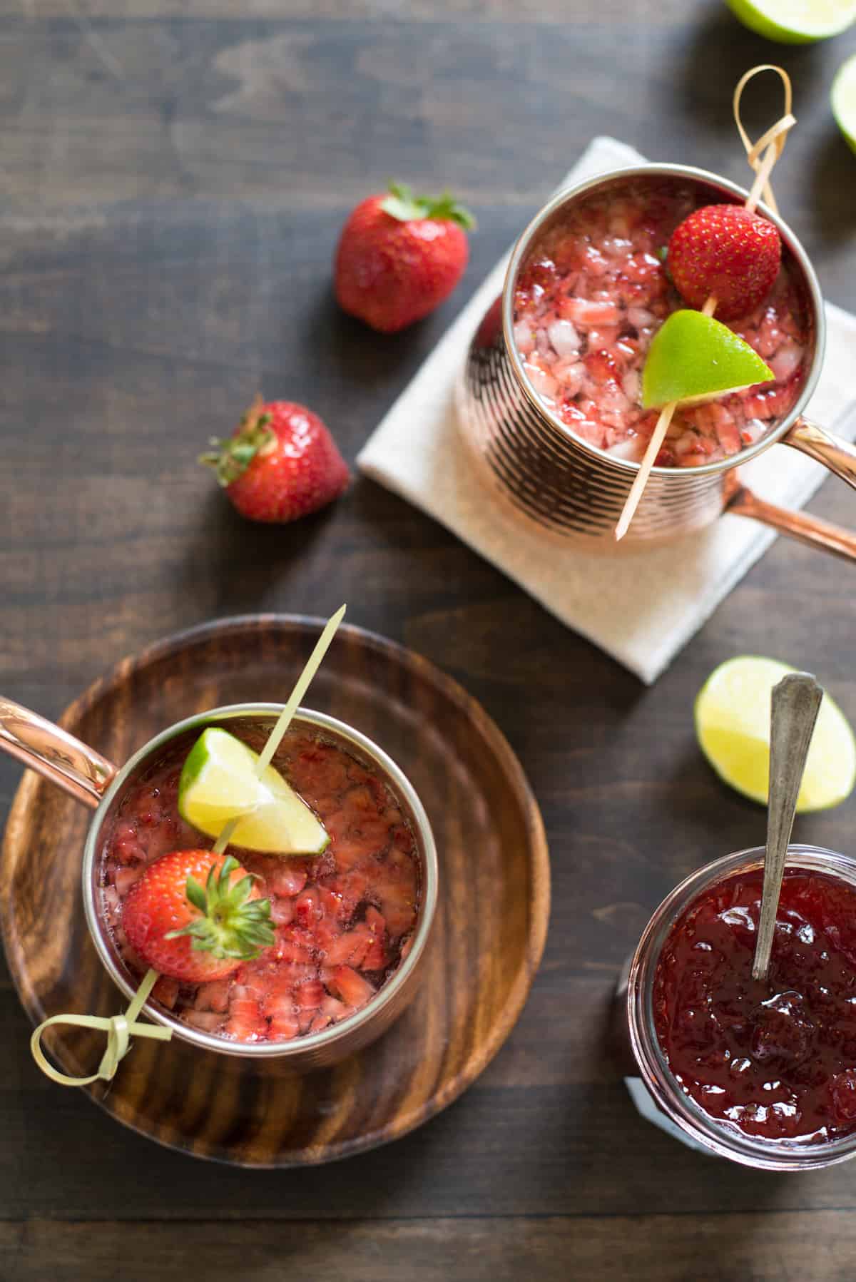 Overhead photo of two strawberry cocktails in hammered copper mugs, with skewers resting on top with strawberries and lime wedges.