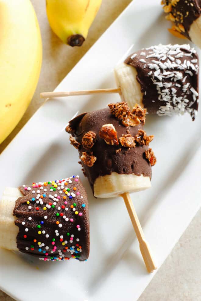 Chocolate covered banana bites on toothpicks on rectangular white tray.