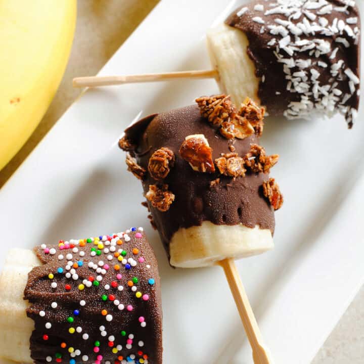 Chocolate covered banana bites on toothpicks on rectangular white tray.