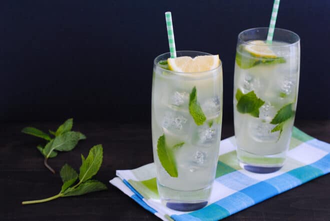 Two tall glasses of an iced lemon drink with mint.