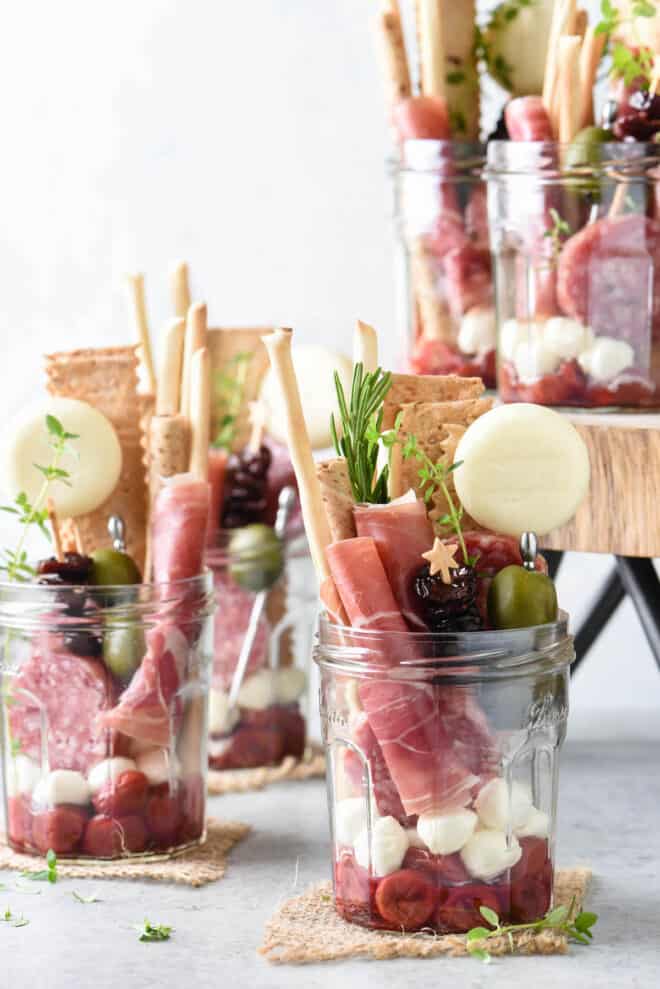 Glass jars filled with charcuterie, cheeses, fruits and crackers.