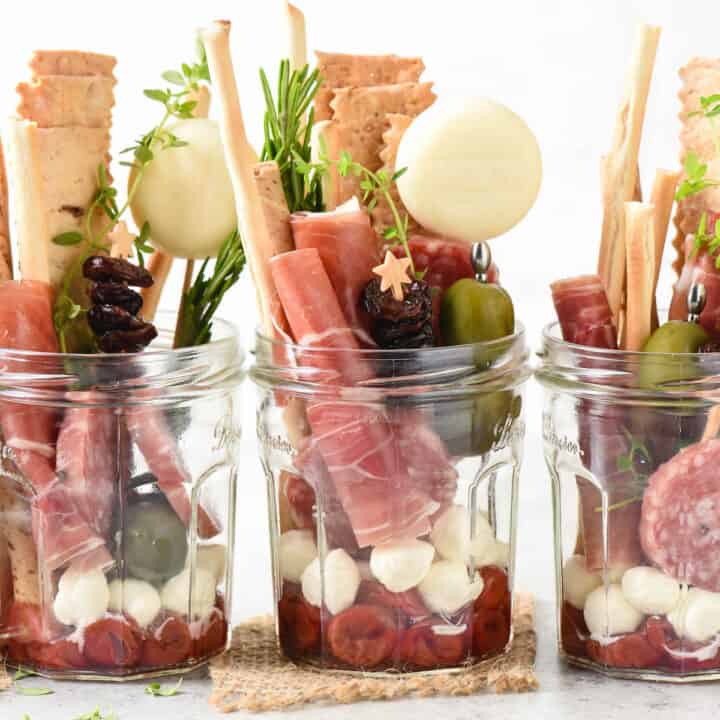 Five servings of jarcuterie, which are glass jars filled with charcuterie, cheese, crackers and condiments.