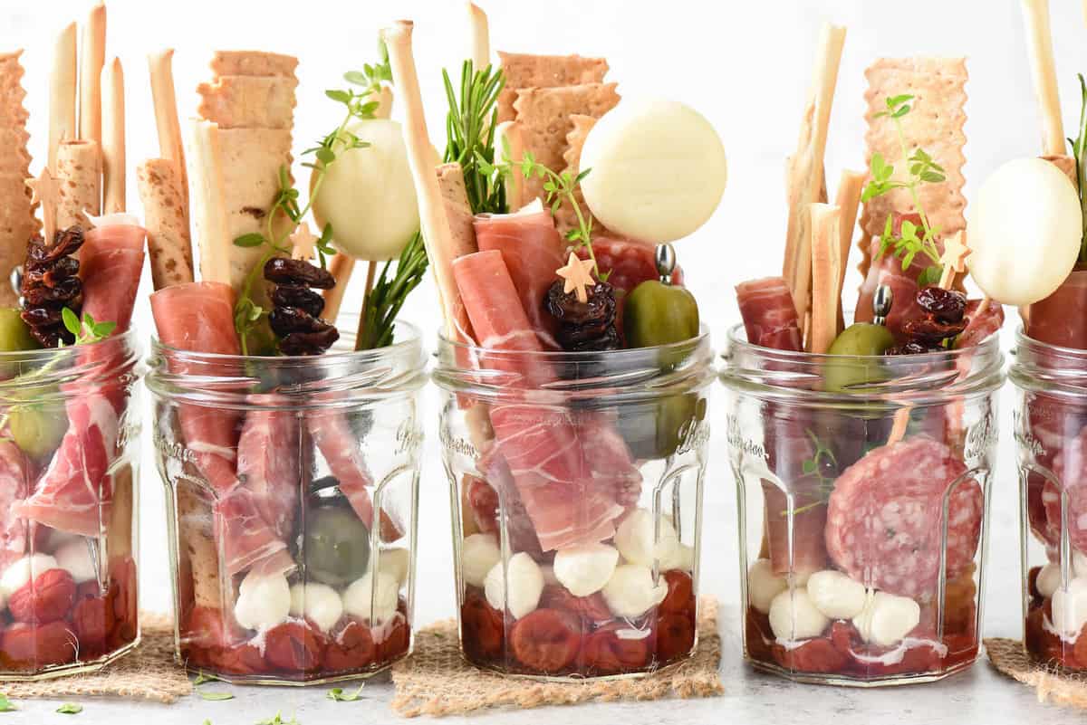 Five servings of jarcuterie, which are glass jars filled with charcuterie, cheese, crackers and condiments.