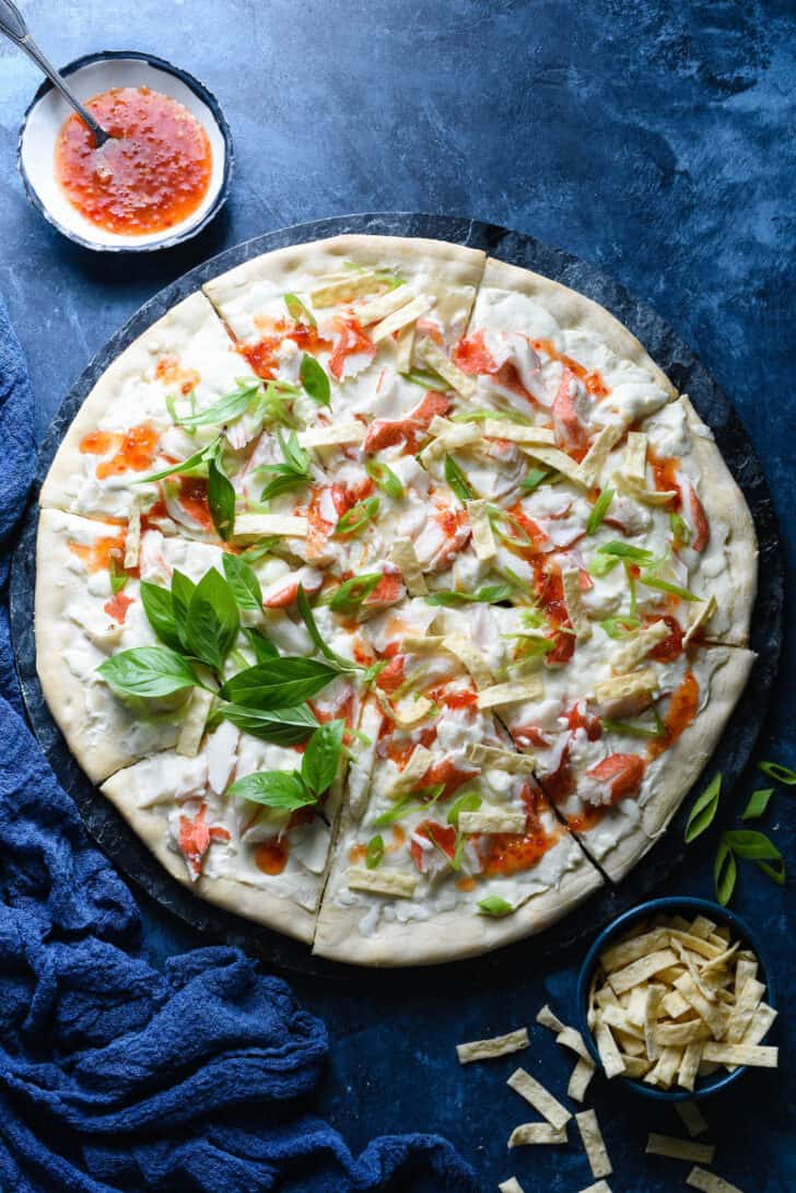Crab pizza topped with sweet chili sauce, Thai basil and wonton strips, on blue background.