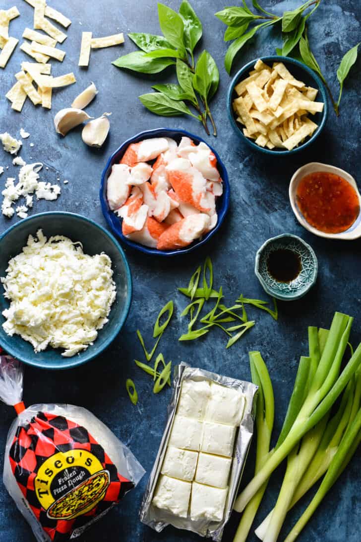 Ingredients needed for crab rangoon pizza, including pizza dough, cream cheese, green onions, mozzarella cheese, imitation crab, wonton strips, garlic, Worcestershire sauce and sweet chili sauce.