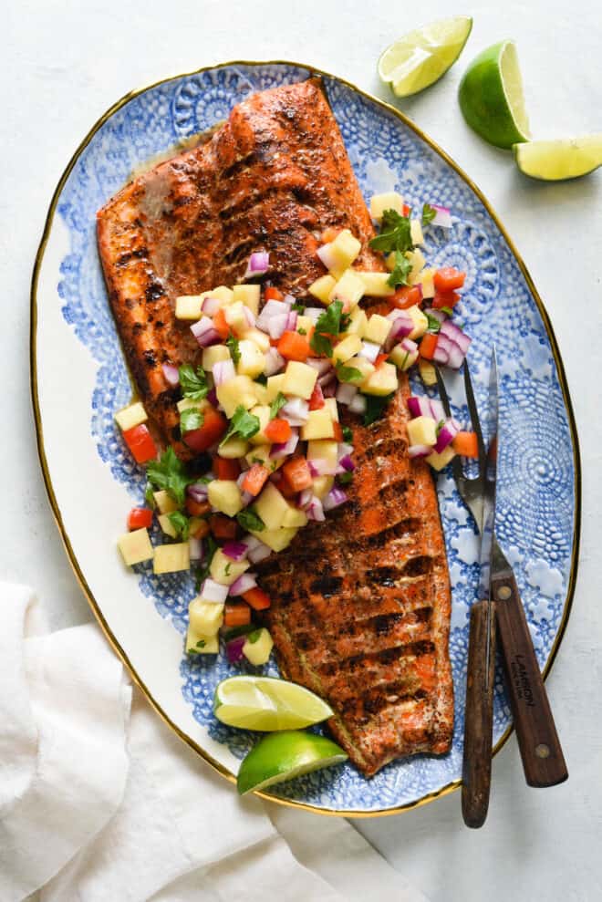 Decorative blue and white platter topped with a large piece of grilled salmon with skin and chopped pineapple salsa.
