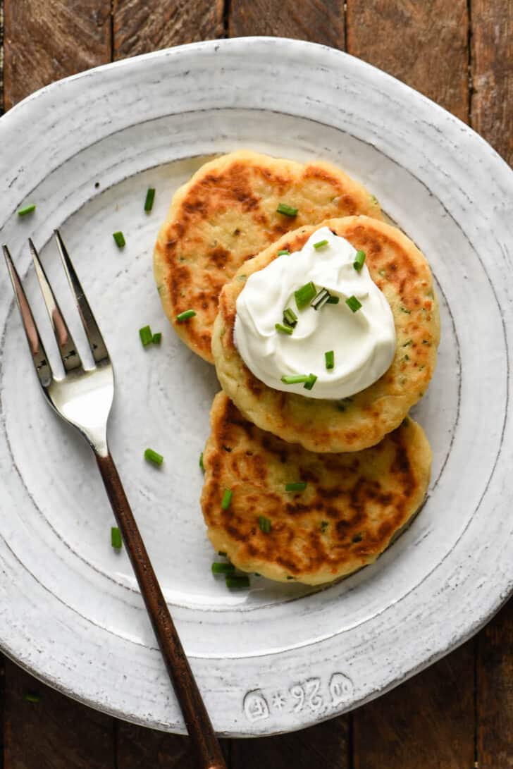 Gray plate topped with three potato cakes from mashed potatoes, garnished with sour cream and chives.
