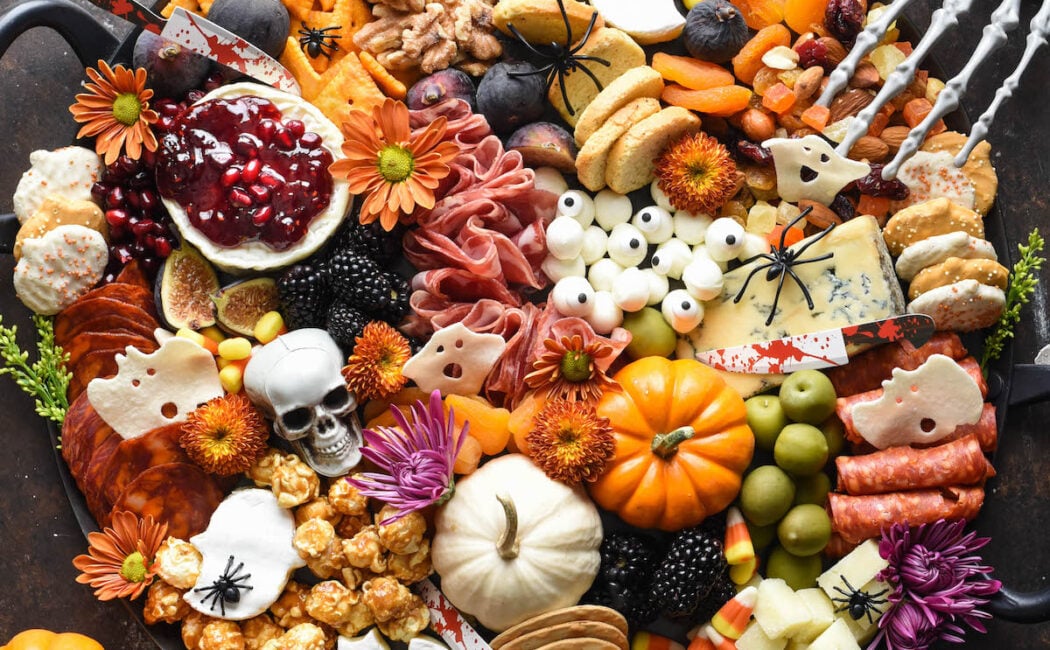 A round Halloween charcuterie board decorated with small pumpkins and seasonal flowers.