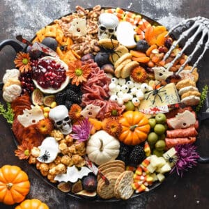 A round Halloween charcuterie board decorated with small pumpkins and seasonal flowers.