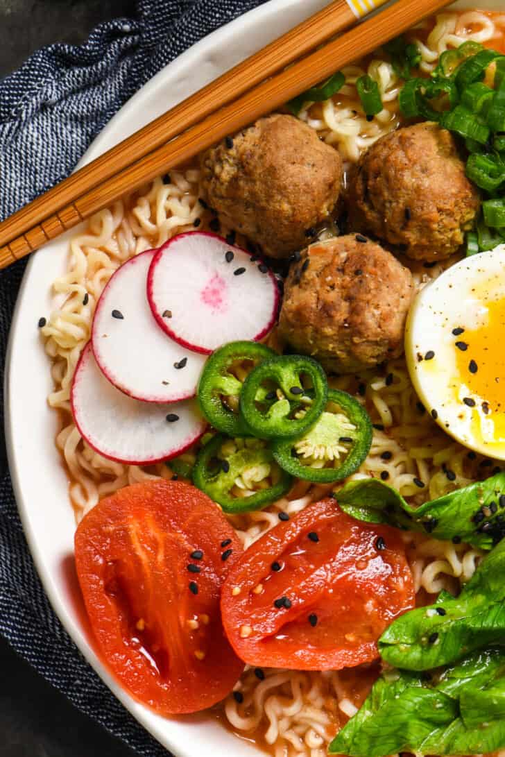 Tomato ramen noodles topped with meatballs, egg, radishes, jalapeno peppers, tomatoes and black sesame seeds.
