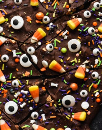 Halloween bark made from chocolate, sprinkles, candy corn and candy eyeballs, broken into pieces, on dark surface.