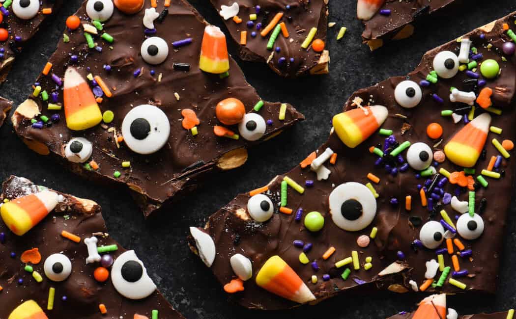 Halloween Bark made with chocolate, candy corn, candy eyeballs and sprinkles, on a dark surface.