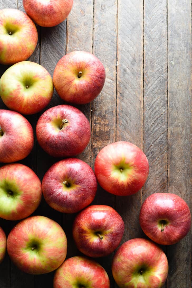 A dozen or so red apples on a planked wooden table, shot from above.